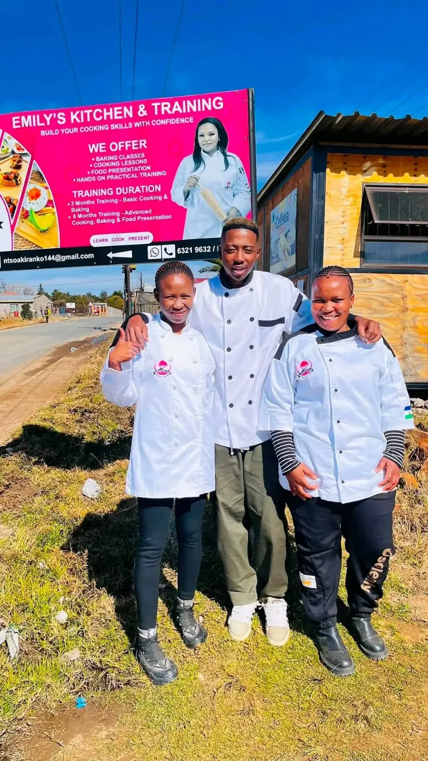 Emily's Kitchen trainees standing below the school billboard